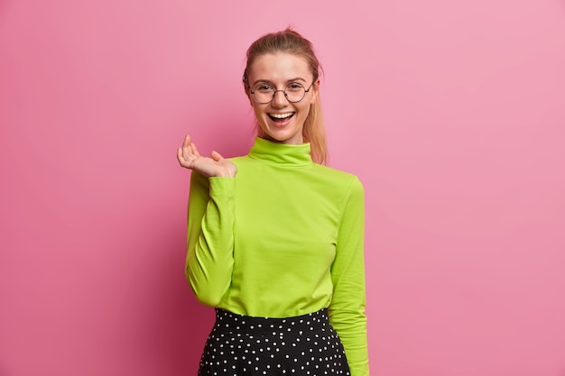 Happy European girl with cheerful expression, laughs at something funny, spends free time in circle of friends, feels ecstatic, dressed in casual green turtleneck. People, emotions, lifestyle