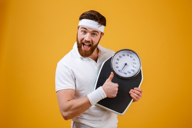 Happy excited bearded fitness man holding weight scales