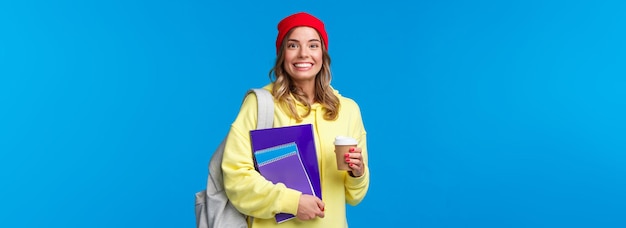 Foto gratuita felice ragazza carina eccitata che inizia l'ultimo anno al college con quaderni e porta caffè da asporto