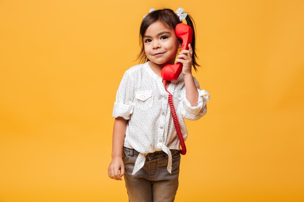 Happy excited little girl talking by red retro telephone.