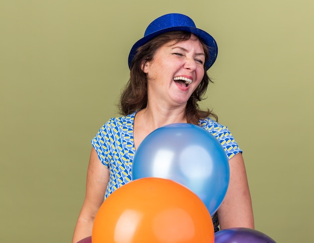 웃고 다채로운 풍선의 무리와 함께 파티 모자에 행복하고 흥분 중년 여성