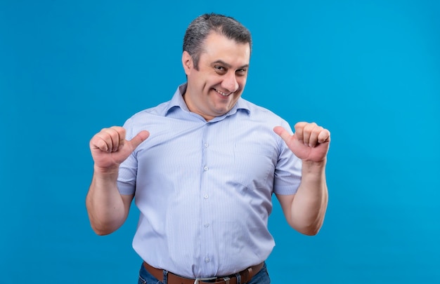 Free photo happy and excited middle-aged man in blue striped shirt pointing at himself and giving call me gesture with hand on a blue space