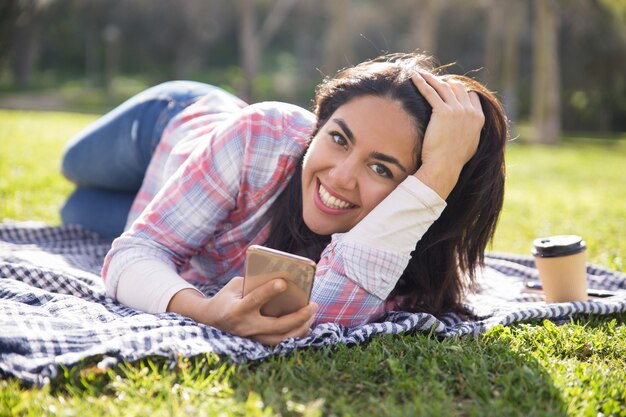 Счастливая взволнованная студентка отдыхает в парке и отправляет сообщения