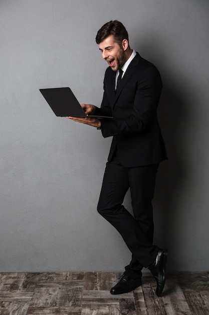 Счастливый возбужденный молодой деловой человек, используя портативный компьютер