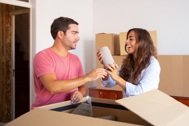 Happy excited young man and woman moving and unpacking things, getting out objects from open carton box