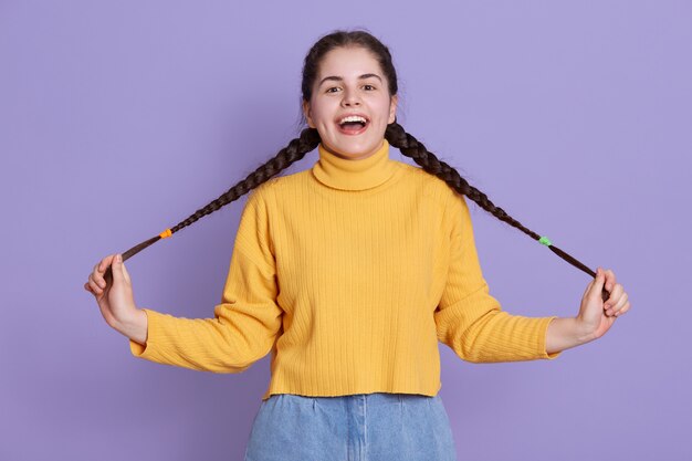 Happy excited young woman with dark long hair, has pigtails, holding and spreading queues aside