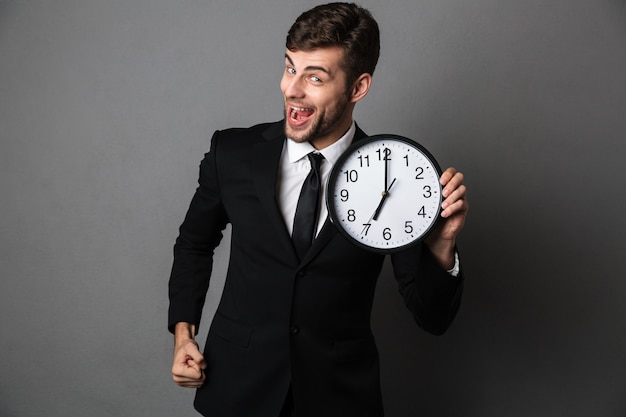 Happy exited bearded man in black suit holding clock, 