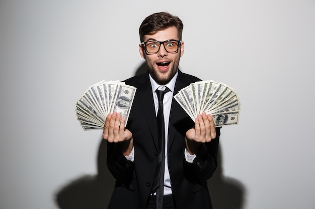 Happy exited man in glasses and black suit holding two bunches of money