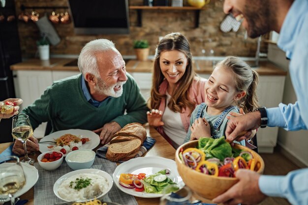 ダイニングルームで昼食時に話している間楽しんでいる幸せな拡大家族フォーカスは小さな女の子にあります