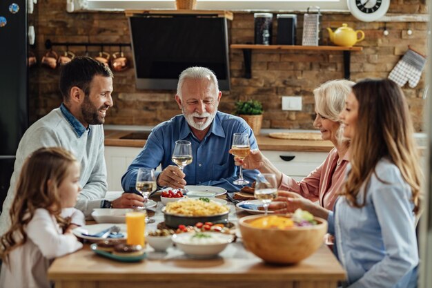 Happy extended family having lunch together in dining room Focus is on senior man