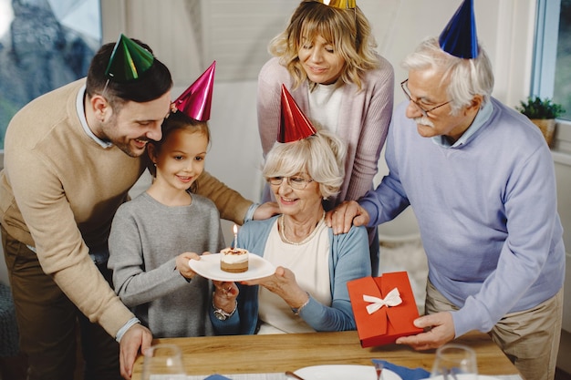 家で誕生日を祝っている間、ケーキで年配の女性を驚かせる幸せな拡大家族