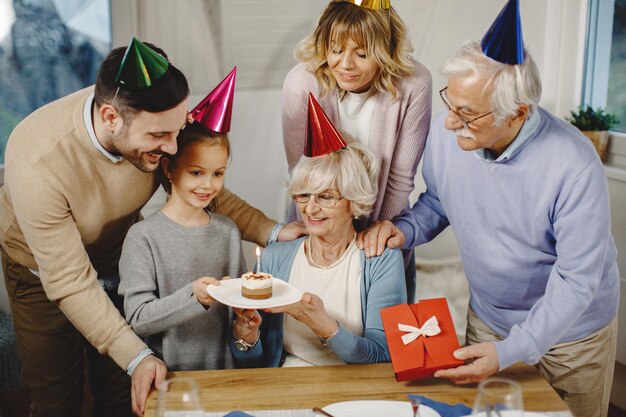 Счастливая расширенная семья удивляет пожилую женщину тортом во время празднования ее дня рождения дома
