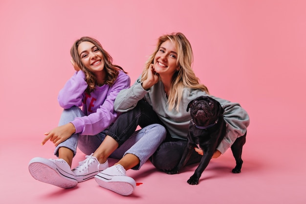 Happy fair-haired girl embracing bulldog puppy. Enchanting female friends relaxing during portraitshoot with pet.