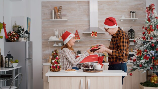 Happy family bringing wrapper christmas present gift with ribbon on it in xmas decorated kitchen