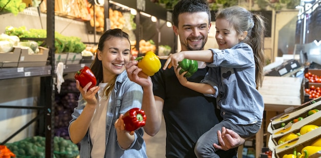 Happy family buys vegetables. Cheerful family of three choosing tomatoes in vegetable department of supermarket or market.