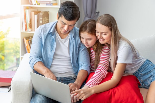 Happy family on couch in living room including father and mother and daughter looking and using notebook