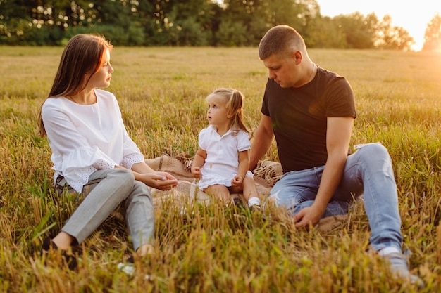 秋の畑で幸せな家族。母、父、赤ちゃんは夕日の光線で自然の中で遊ぶ