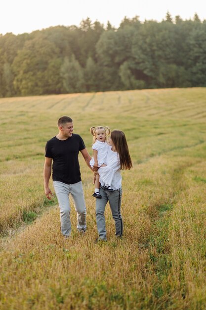 秋の畑で幸せな家族。母、父、赤ちゃんは夕日の光線で自然の中で遊ぶ