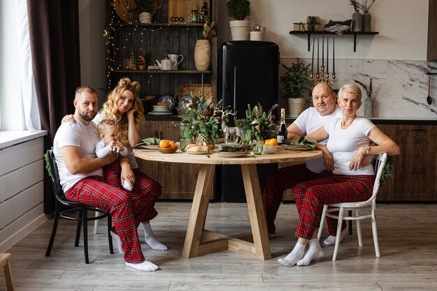 Happy family of four adults and a baby celebrating New Year together in the kitchen at round table.