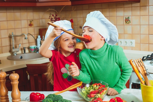 Happy family funny kids are preparing the a fresh vegetable salad in the kitchen