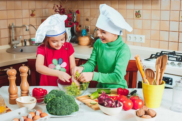 幸せな家族の面白い子供たちが準備している、キッチンで新鮮な野菜サラダ