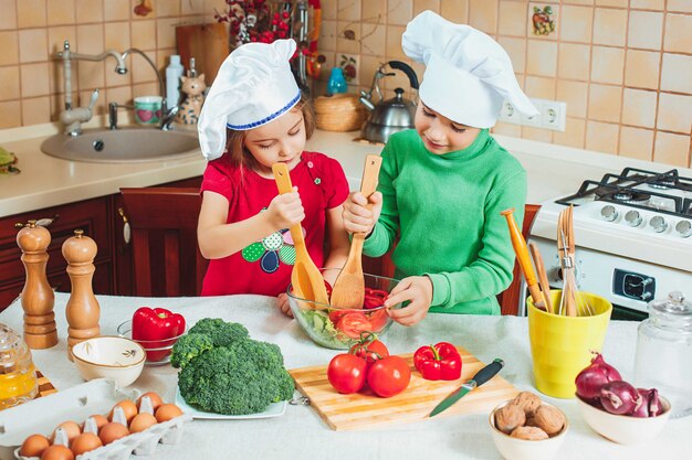 Happy family funny kids are preparing the a fresh vegetable salad in the kitchen