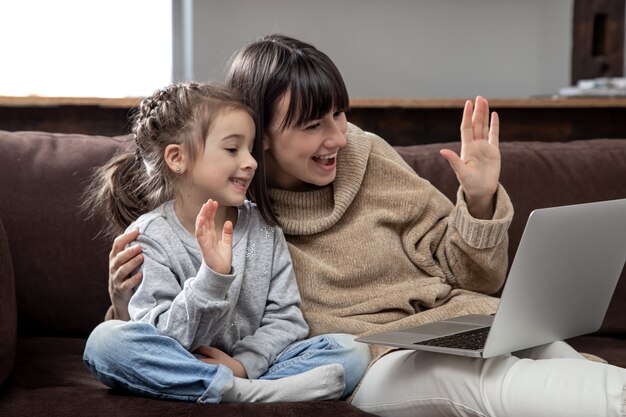 Happy family looking at laptop screen make distance video call. Smiling mother and little girl talking to webcamera on internet chat.