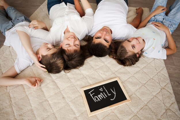 Happy family lying on carpet near slate with family text at home