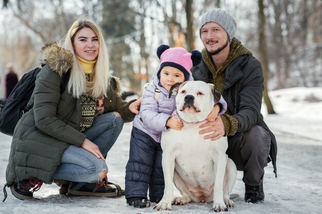 母親、お父さん、小さな娘の幸せな家族が公園にアメリカのブルドッグと一緒に姿を現す