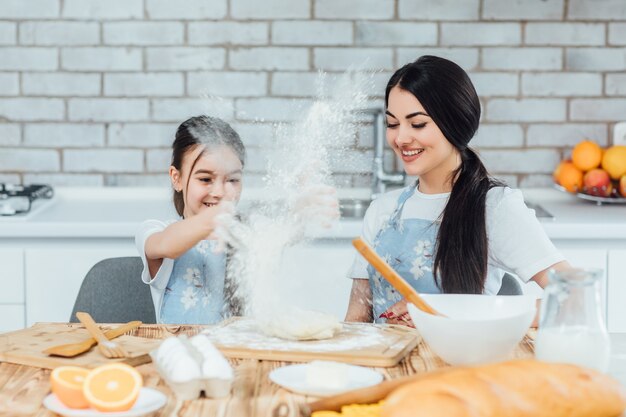 Happy family mother and child daughter bake kneading dough in the kitchen