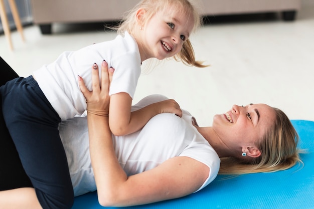 Happy family of mother and daughter at home on yoga mat