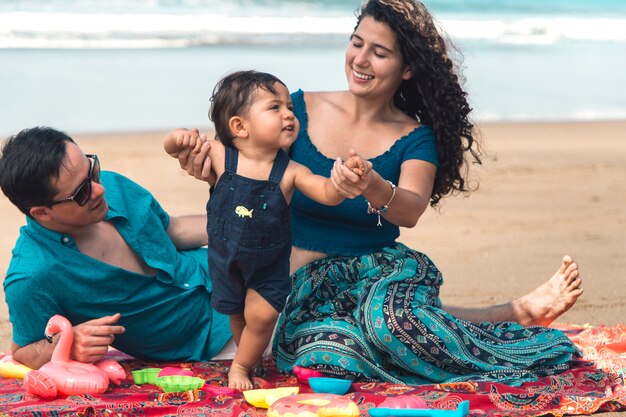 Happy family playing and baby learning to walk on beach