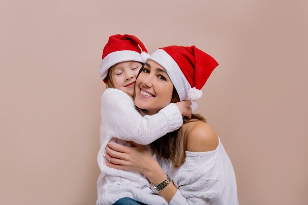 Happy family portrait of adorable mother with daughter preparing for christmas party wearing santa's caps.