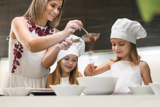 母が台所でストレーナーを通してココアパウダーをふるいながら食べ物を準備する幸せな家族