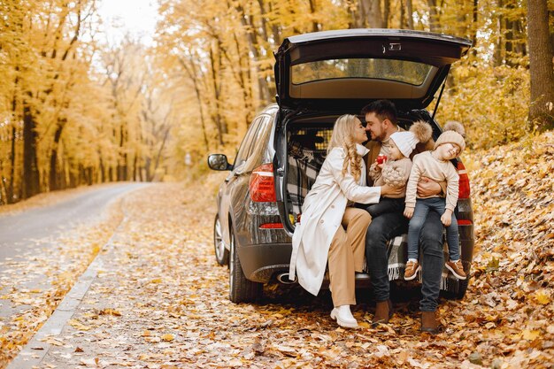 가을 공원에서 야외 활동을 한 후 행복한 가족이 쉬고 있습니다. 아버지, 어머니, 그리고 차 트렁크 안에 앉아 있는 두 아이가 웃고 있습니다. 가족 휴가 및 여행 개념입니다.
