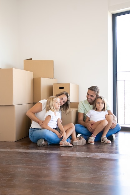 Happy family sitting near carton boxes in living room of new home