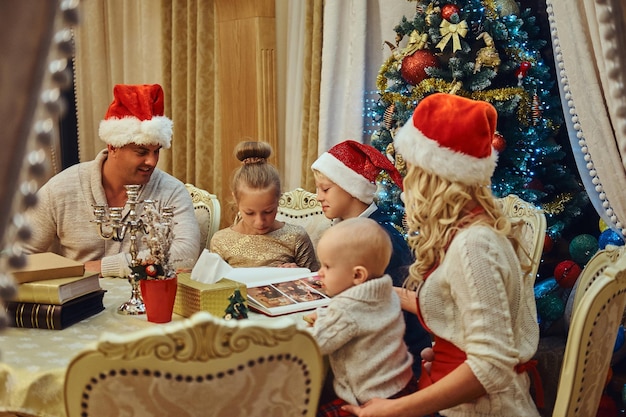 Famiglia felice seduta insieme a tavola in un elegante soggiorno decorato per natale, guarda le foto di famiglia