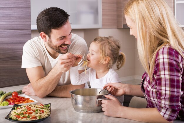 행복한 가족과 그들의 어린 딸이 부엌 카운터에서 스파게티를 먹고 있다