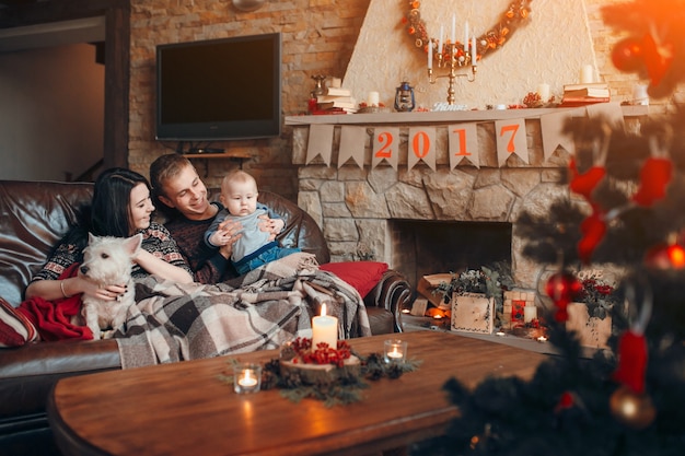 Happy family with a baby and a dog and beside him a chimney with the poster of 2017