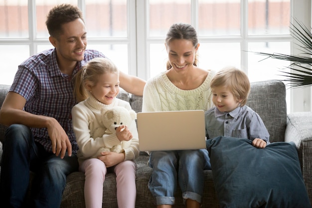 Happy family with children having fun using laptop on sofa