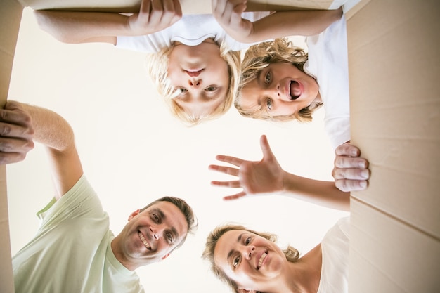 Happy family with cute children opening moving cardboard box and looking inside