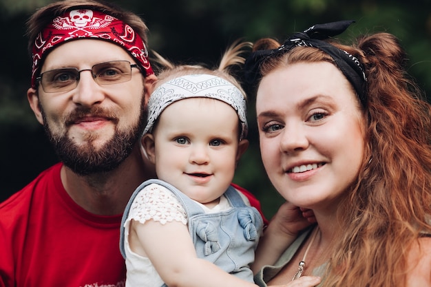 Famiglia felice con la ragazza che ride in posa insieme all'aperto sullo sfondo dell'albero verde. madre e padre sorridenti che tengono in braccio i bambini che si godono la genitorialità