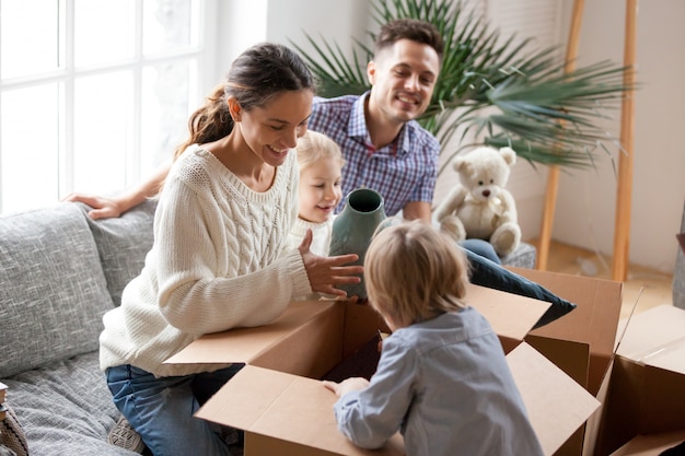 Счастливая семья с детьми распаковывает коробки, переезжает в новый дом