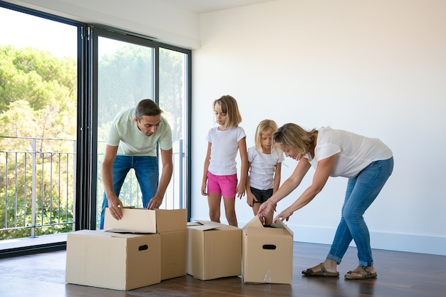 Счастливая семья с двумя детьми, распаковывая коробки в новом доме