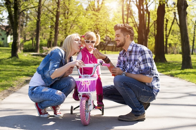 Happy family with young caucasian parents teaching their daughter how to ride a bike