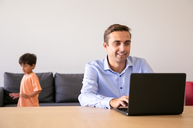 소년 그 근처에서 놀 때 인터넷에서 검색하는 행복 한 아버지. 랩톱 컴퓨터를 사용하고 집에서 일하는 백인 아빠.