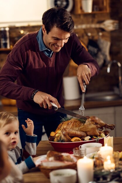 Happy father carving turkey during Thanksgiving dinner in dining room