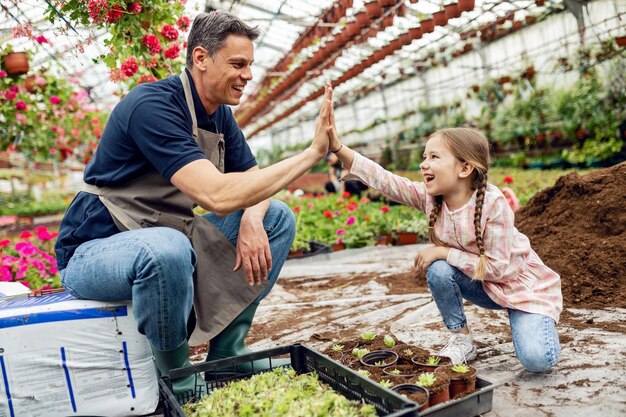 植物保育園で花を植えた後、ハイファイブを与える幸せな父と娘