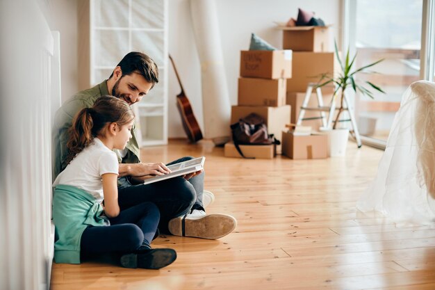 Happy father and daughter looking at photo album while relocating in new home