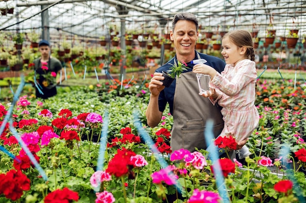 幸せな父と娘は鉢植えの花に栄養を与え、温室でそれらに水をまきます